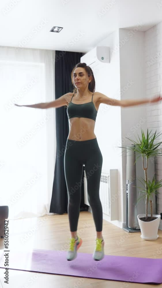 Vertical Screen: Fit woman in sportswear jumping in living room in slow motion. Active female staying at home and training during lockdown. Healthy lifestyle. Concept of fitness Vertical Screen: Fit woman in sportswear jumping in living room in slow motion. Active female staying at home and training during lockdown. Healthy lifestyle. Concept of fitness