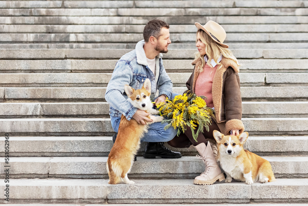 A young couple in love on a date in the park. A blonde in a hat and a man look at each other. Walking with corgi dogs. Spring