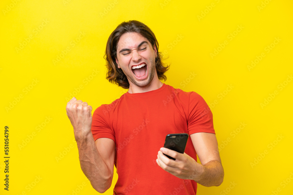 Caucasian handsome man isolated on yellow background with phone in victory position Caucasian handsome man isolated on yellow background with phone in victory position