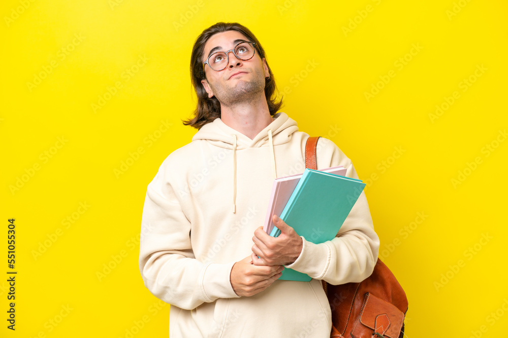 Young student handsome man isolated on yellow background and looking up Young student handsome man isolated on yellow background and looking up