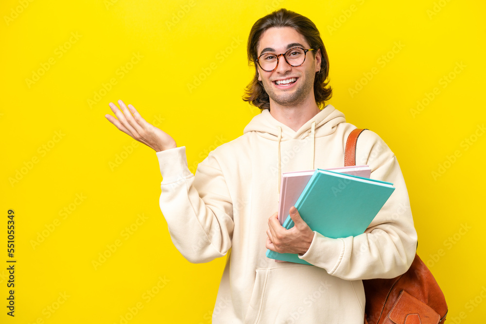 Young student handsome man isolated on yellow background extending hands to the side for inviting to come Young student handsome man isolated on yellow background extending hands to the side for inviting to come