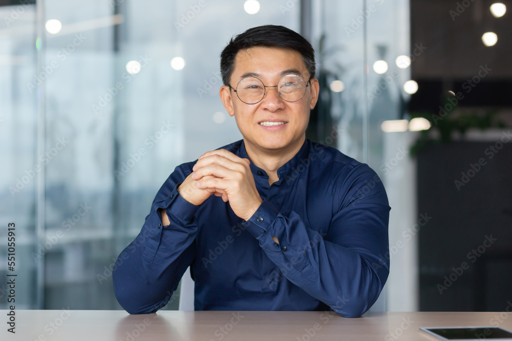 Φωτογραφία Young successful Asian businessman looking at caper and smiling, video call sitting at table investor boss in shirt and glasses