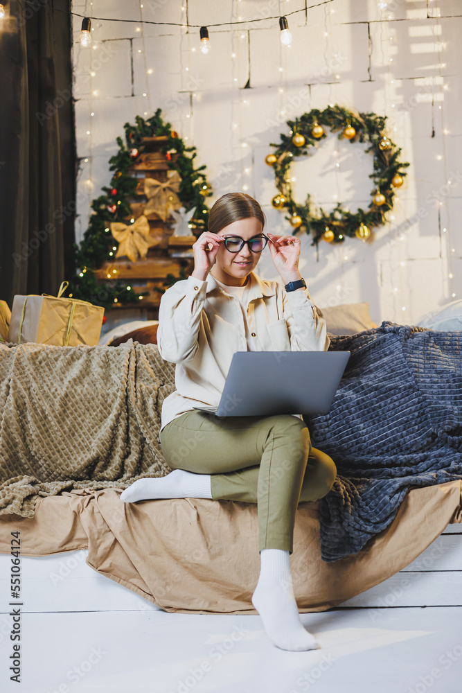 Obraz premium Beautiful Merry Christmas woman drink a sweet cup of hot cocoa, wear comfortable home clothes, look at the laptop, work remotely for the new year, plaid, New Year's winter mood.