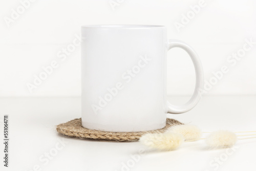 Mockup of white mug on table with jute coaster and dried flowers, neutral color. Blank coffee cup mug mock up in Boho style.