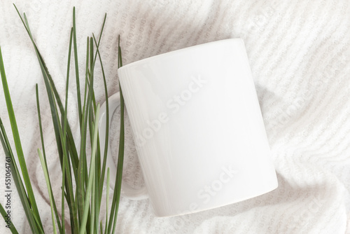 Mockup of white mug on knitted plaid with greenery. Blank coffee cup mug mock up, flat lay.