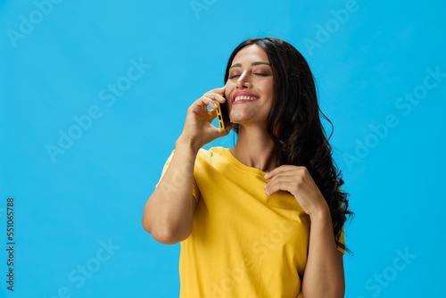 Woman with a phone in her hands with a yellow case on a blue background in a yellow T-shirt, emotions signals gestures, online lifestyle concept, shopping, communication, learning, business online