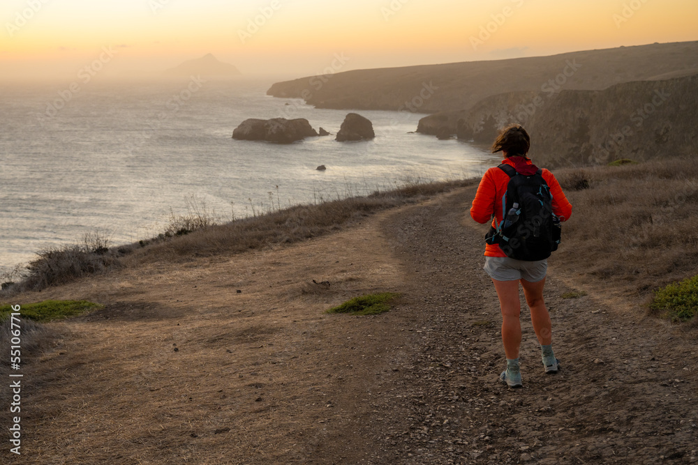 Woman With Backpack and Orange Coat Looks Out At Sunrise Over Santa Cruz Island Toward Anacapa Island