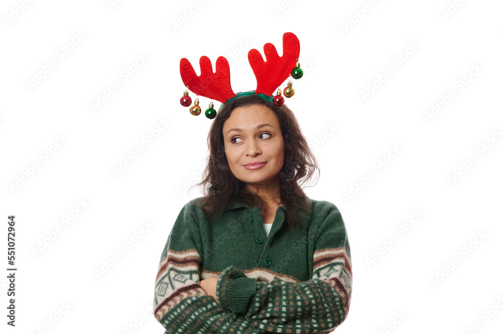 Latin American pretty woman in green sweater and deer antler hoop, thoughtfully looking aside at copy space on white background, posing with her arms crossed. Free space for your advertising text Latin American pretty woman in green sweater and deer antler hoop, thoughtfully looking aside at copy space on white background, posing with her arms crossed. Free space for your advertising text