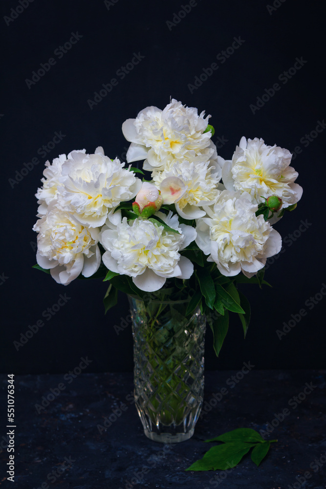 Beautiful white peony flowers bouquet with water drops on petals in glass vase with dark background Beautiful white peony flowers bouquet with water drops on petals in glass vase with dark background
