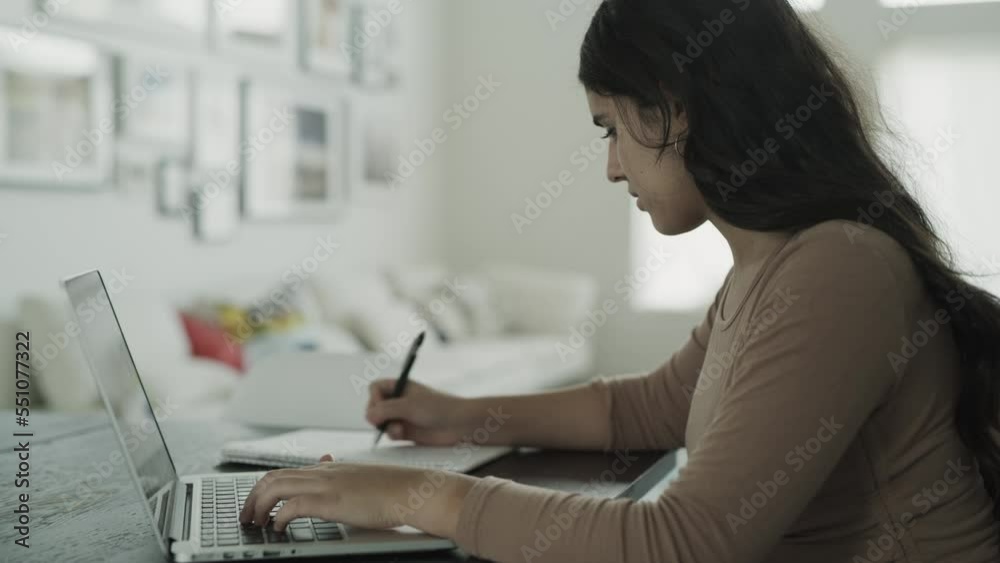 Close up of teenage girl using laptop for online school and taking notes / Lehi, Utah, United States Close up of teenage girl using laptop for online school and taking notes / Lehi, Utah, United States