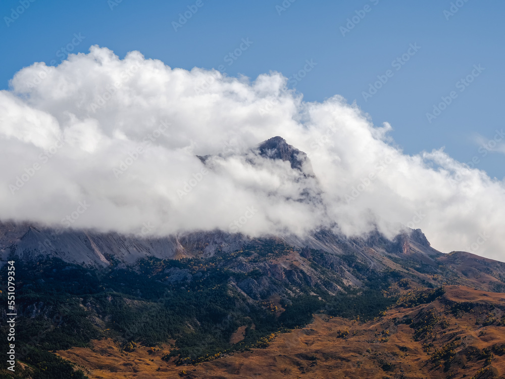 Scenic landscape with autumn mountain valley against large mountains in low clouds in morning sunlight. Vivid hillside with view to sunlight high mountain range in low clouds.
