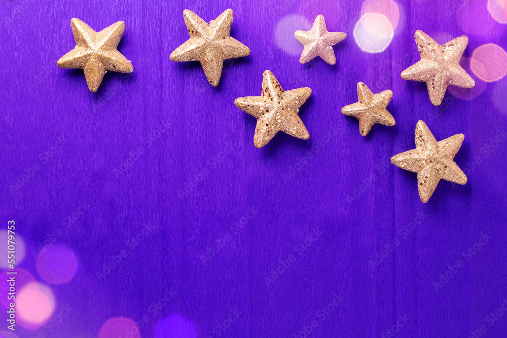 Postcard with big and small golden decorative stars and bokeh light on violet paper textured background. Top view. Christmas, New Year holidays concept. Place for text. Postcard with big and small golden decorative stars and bokeh light on violet paper textured background. Top view. Christmas, New Year holidays concept. Place for text.