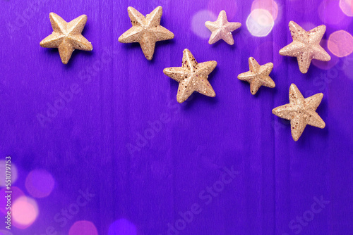 Postcard with big and small golden decorative stars and bokeh light on violet paper textured background. Top view. Christmas, New Year holidays concept. Place for text.