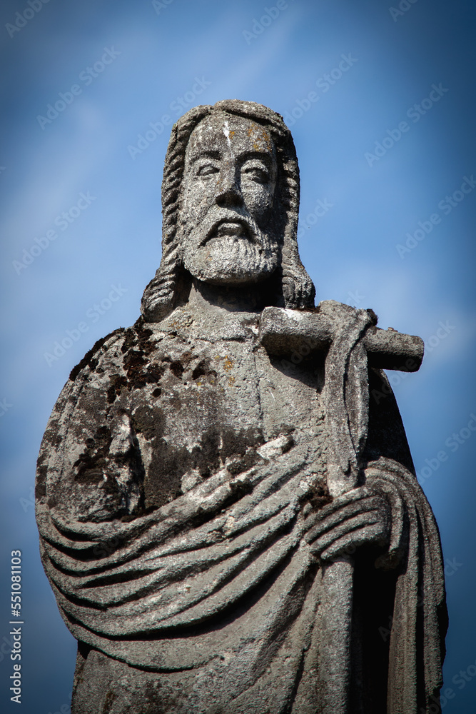Stone statue of the apostle with broken cross against blue sky