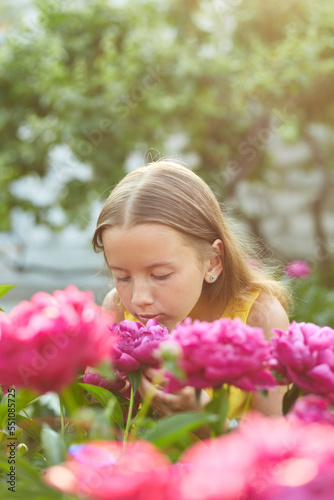 Happy little girl with braces in the garden in bushes of peonies