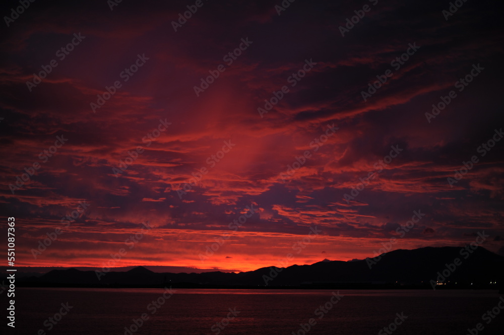 Red, pink, orange and violet sunrise at the seaside during dawn with clouds in the sky and mountains on the shore of a port