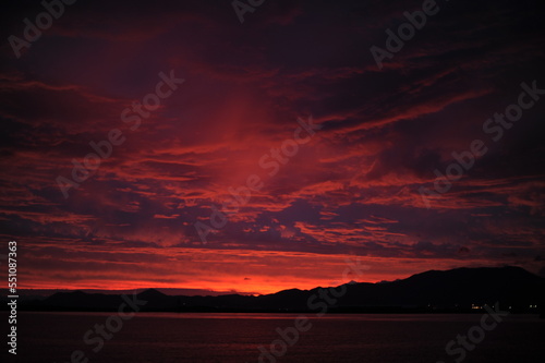 Red  pink  orange and violet sunrise at the seaside during dawn with clouds in the sky and mountains on the shore of a port