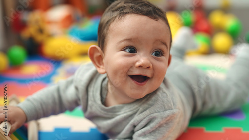 Adorable hispanic baby smiling confident lying on floor at kindergarten