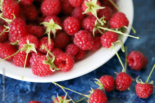Fresh raspberries with tails on a white plate. Close-up.
