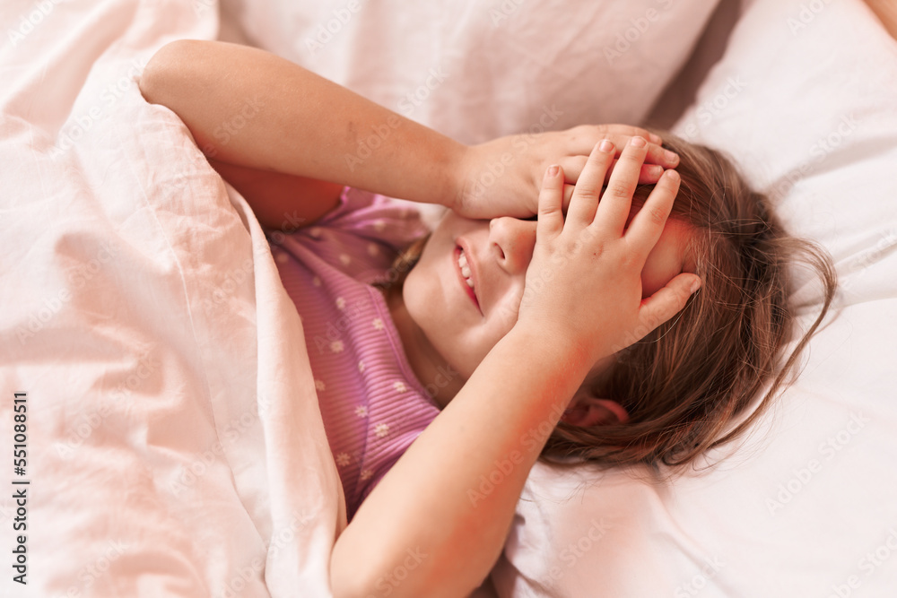 Adorable hispanic girl stressed with hands on eyes lying on bed at bedroom