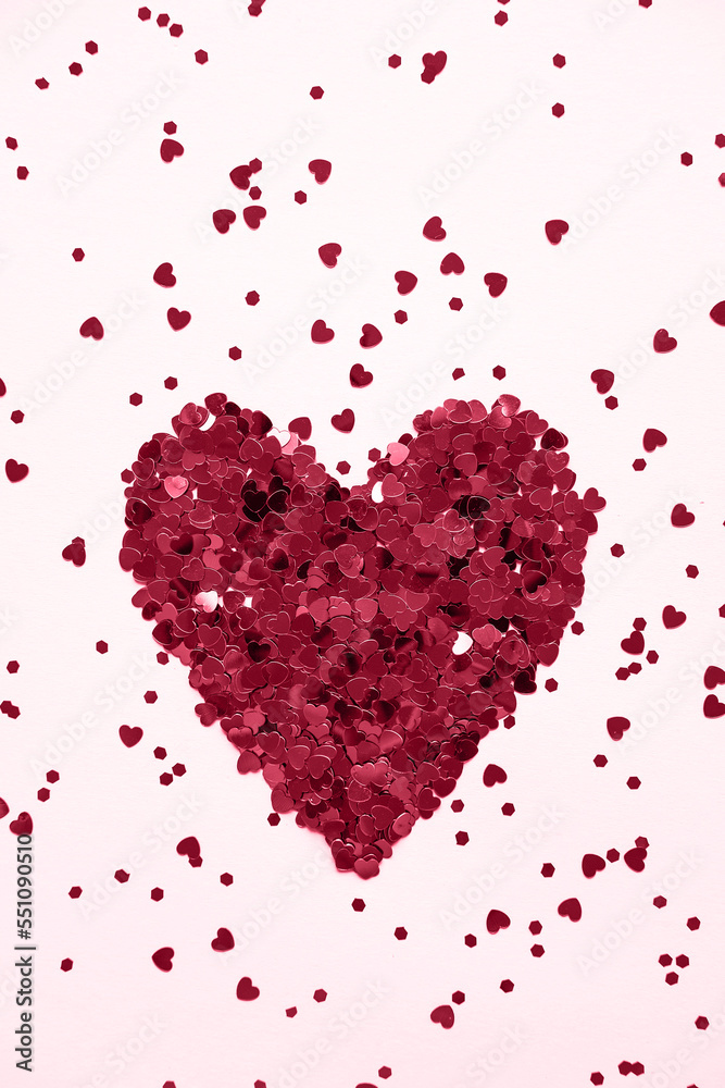 Valentine's day background. Heart made of shiny red small decorative hearts on a pink background strewn with sparkles. Demonstrating the colors of 2023 Viva Magenta. Vertical image, flat lay.