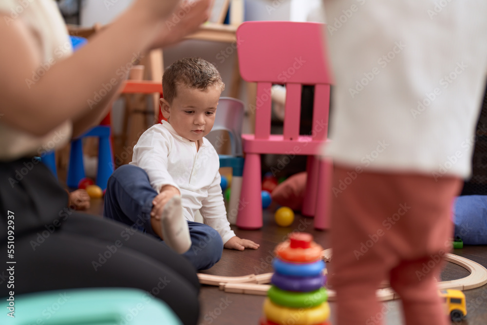 Adorable toddler sitting on floor with relaxed expression at kindergarten