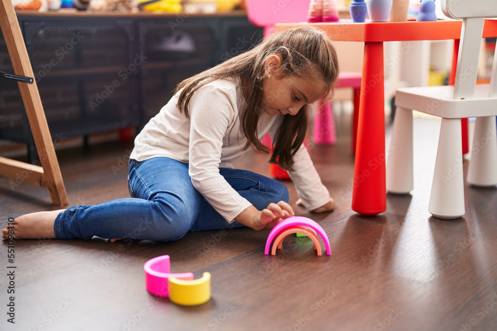 Adorable hispanic girl playing with toys sitting on floor at kindergarten Adorable hispanic girl playing with toys sitting on floor at kindergarten
