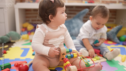 Two toddlers playing with toys sitting on floor at kindergarten