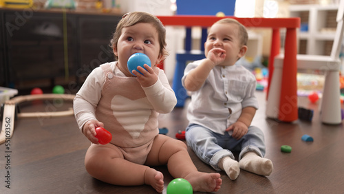Two toddlers sucking ball sitting on floor at kindergarten
