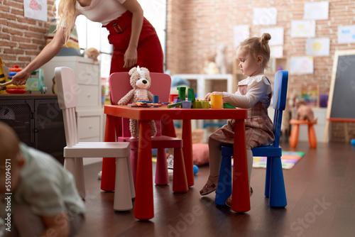 Adorable caucasian girl playing with toys sitting on table at kindergarten