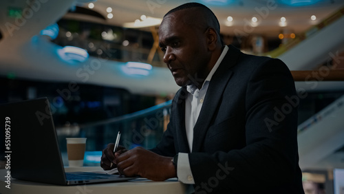African middle-aged adult businessman worker entrepreneur man boss leader specialist company CEO freelancer teacher working with laptop writing notes in notebook check data in computer write in cafe