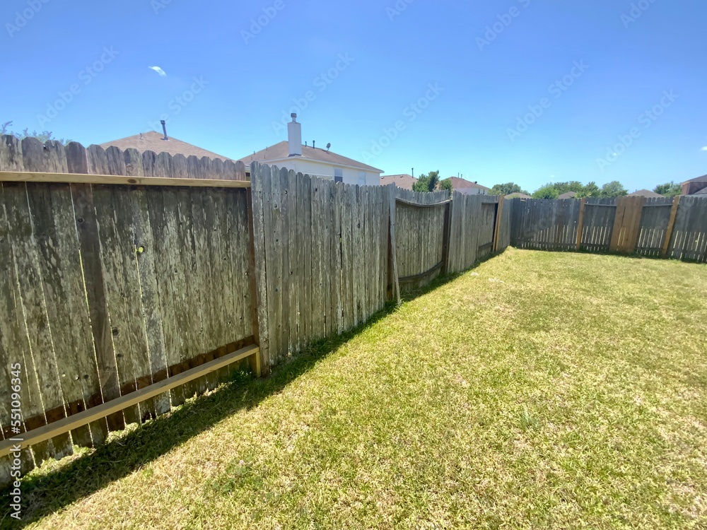 Large suburban backyard with a rustic old wood fence, trimmed grass, set against neighboring homes under a clear blue sky. Large suburban backyard with a rustic old wood fence, trimmed grass, set against neighboring homes under a clear blue sky.