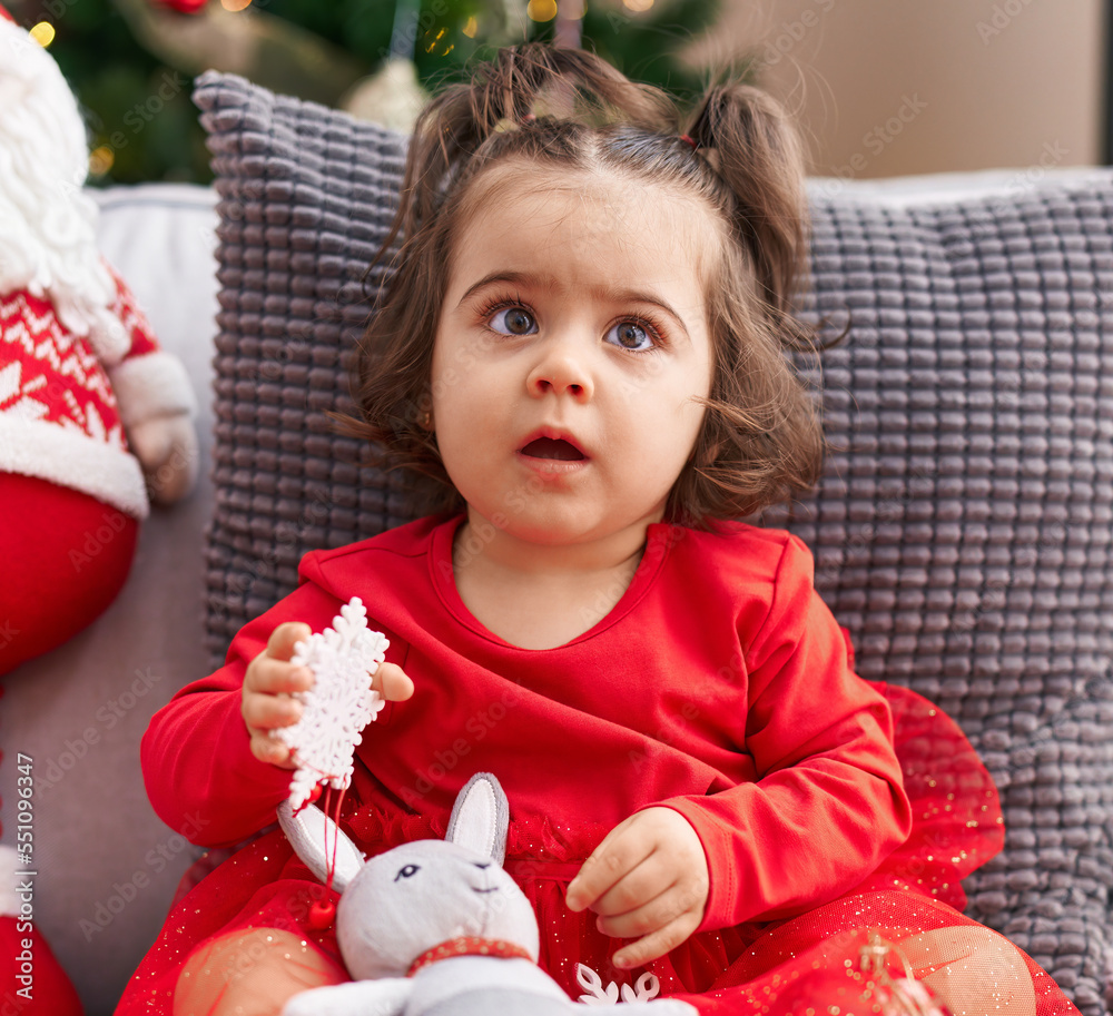 Adorable hispanic girl sitting on sofa by christmas tree at home Adorable hispanic girl sitting on sofa by christmas tree at home