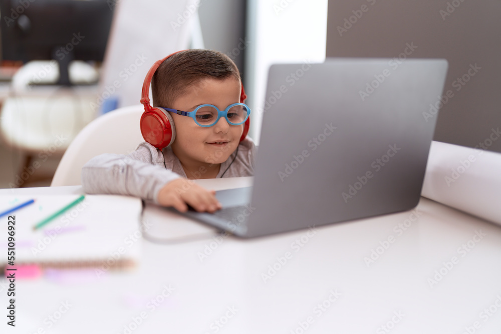 Adorable hispanic toddler student using laptop and headphones studying at classroom Adorable hispanic toddler student using laptop and headphones studying at classroom