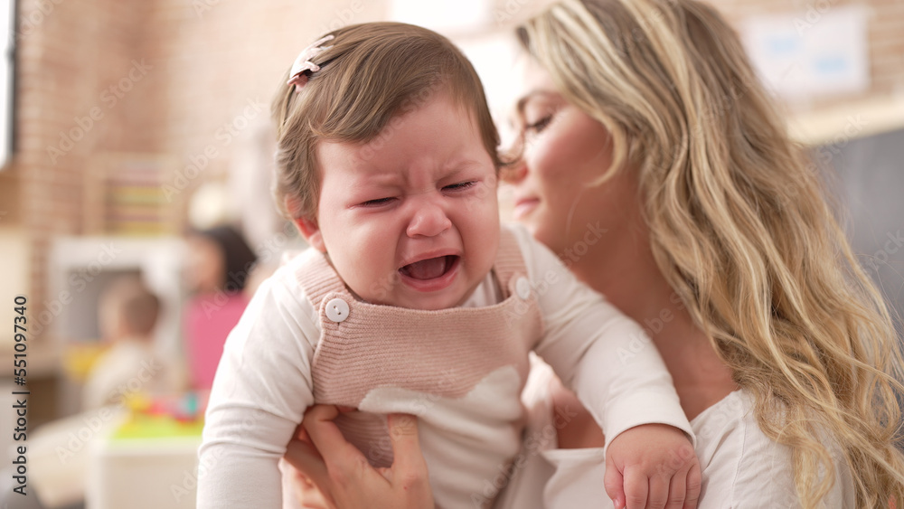 Mother and daughter consueling baby crying at kindergarten Mother and daughter consueling baby crying at kindergarten