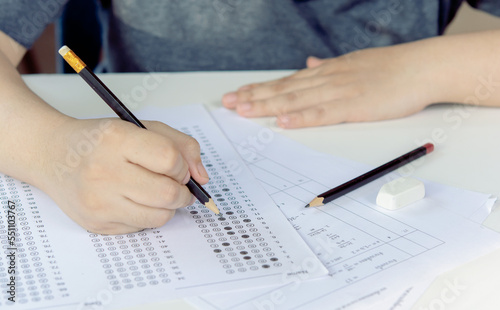 Students hand holding pencil writing selected choice on answer sheets and Mathematics question sheets. students testing doing examination. school exam