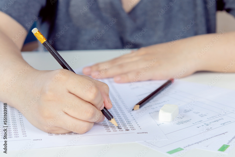 Students hand holding pencil writing selected choice on answer sheets and Mathematics question sheets. students testing doing examination. school exam Students hand holding pencil writing selected choice on answer sheets and Mathematics question sheets. students testing doing examination. school exam