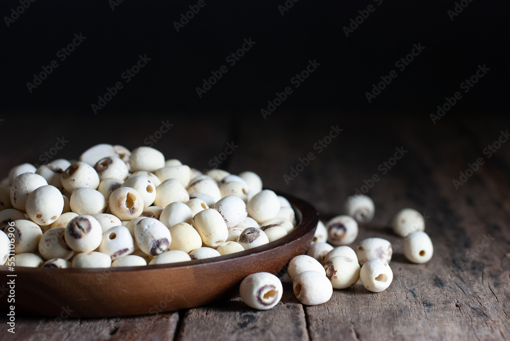 Dried lotus seeds in a wooden tray on a rustic wooden floor, selective focus.