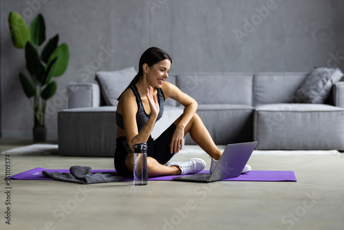Video call to sports coach on a distance, training online. A young woman sits on the floor and talking with a coach by laptop