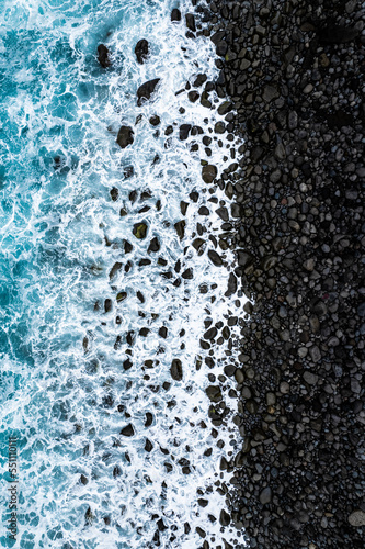 Aerial View of rocky Miradouro Ilheus da Ribeira da Janela in Madeira island with waves crashing on black stones