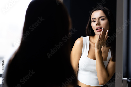 Smiling young woman touching face and looking at mirror in bathroom