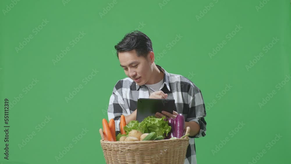 Asian Male Farmer With Vegetable Basket Writing Tablet On Green Screen Background In The Studio
