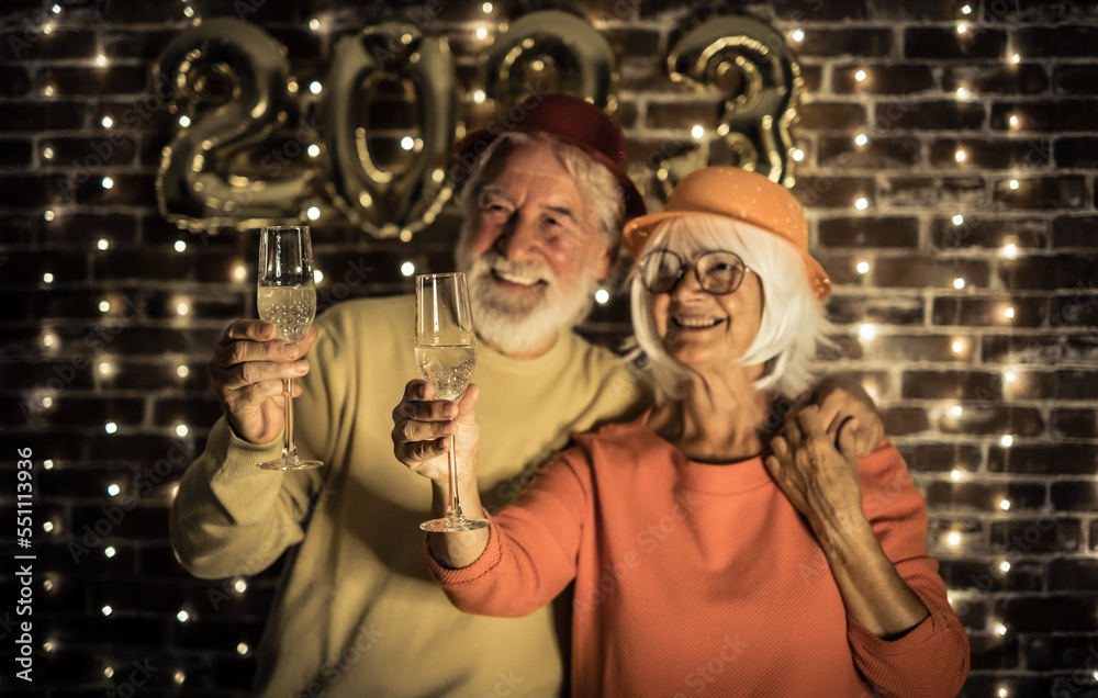 Obraz premium Blurred cheerful senior couple holding champagne flutes having party by night. Happiness lifestyle for mature retired people waiting for new year 2023