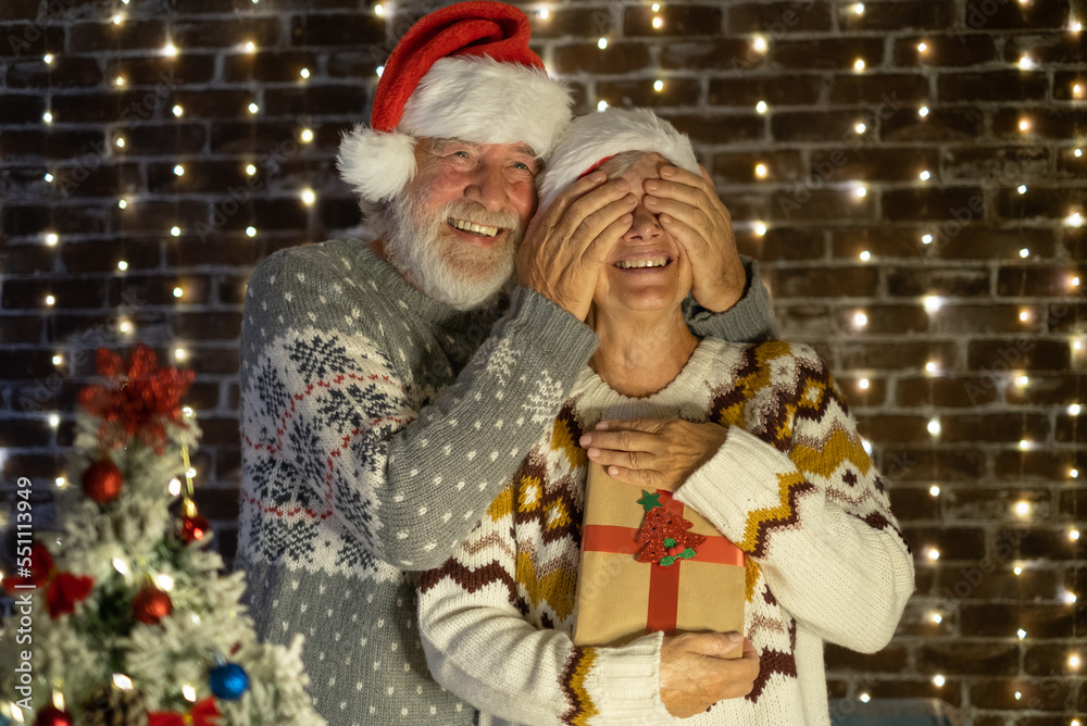 Surprise for her. Christmas event and celebration. Happy Senior couple with Santa hats exchange a present