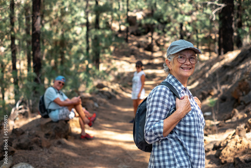 Beautiful caucasian senior woman with hat and backpack walking with friends on a mountain hike enjoying free time and freedom in nature, seniors retired and healthy lifestyle concept