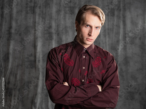 an attractive man in an elegant suit, burgundy shirt with embroidery. Photo in the studio on a gray background