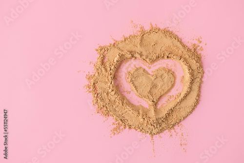 Top view of heart shape made of raw maca root powder on soft pink background with copy space photo