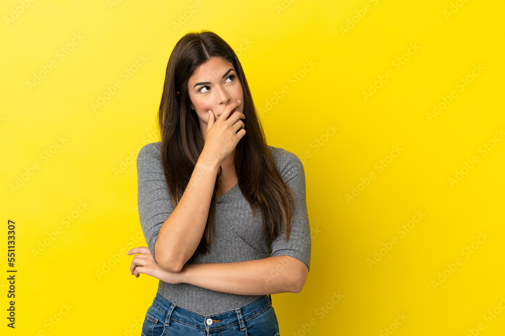 Young Brazilian woman isolated on yellow background having doubts and with confuse face expression Young Brazilian woman isolated on yellow background having doubts and with confuse face expression