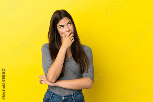 Young Brazilian woman isolated on yellow background having doubts and with confuse face expression © luismolinero