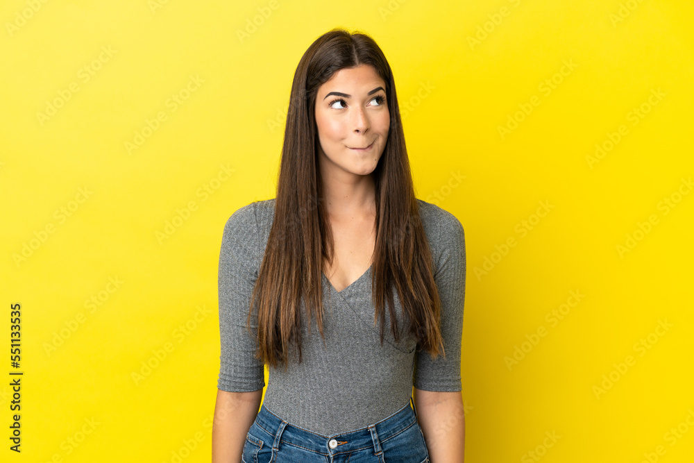 Young Brazilian woman isolated on yellow background having doubts while looking up Young Brazilian woman isolated on yellow background having doubts while looking up